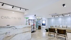 Eine moderne Hotelhalle mit einem Marmor-Empfangstresen, einer Sitzecke mit Sofas und Sesseln sowie einem großen Fenster mit Vorhängen.