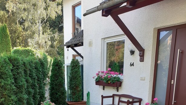 A well-maintained garden with a bench and potted plants near a building entrance. - Chic apartment between Munich and Lake Starnberg (Gauting)