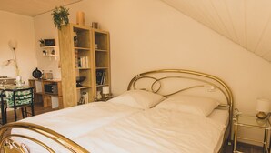 A bedroom with a bed, a wooden bookshelf, a desk, and a dining area. - Chic apartment between Munich and Lake Starnberg (Gauting)