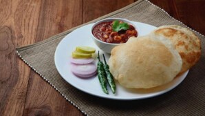 Ein Teller mit einem Brötchen, einer Schale Chutney, Scheiben Zwiebeln und grünen Chilis.