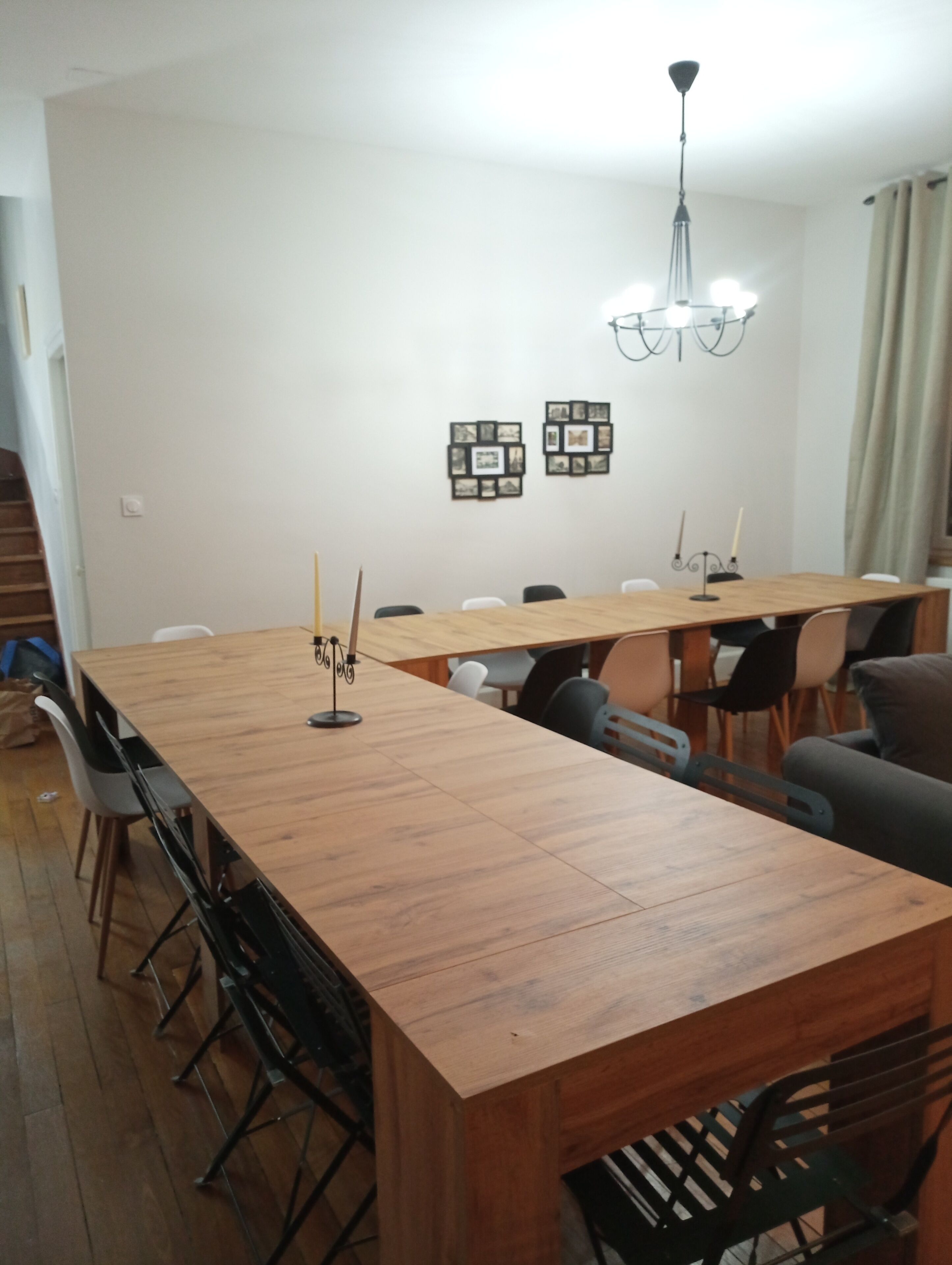 A dining area with a long wooden table, chairs, a chandelier, and framed pictures on the wall.