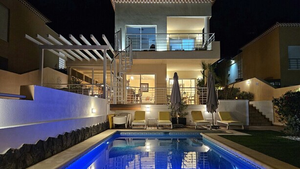 Ein zweistöckiges Haus mit Swimmingpool, Sitzgelegenheiten im Freien und einer Pergola.