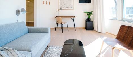 A modern living room with a sofa, a coffee table, a desk with a chair, a TV, and a window with a city view.