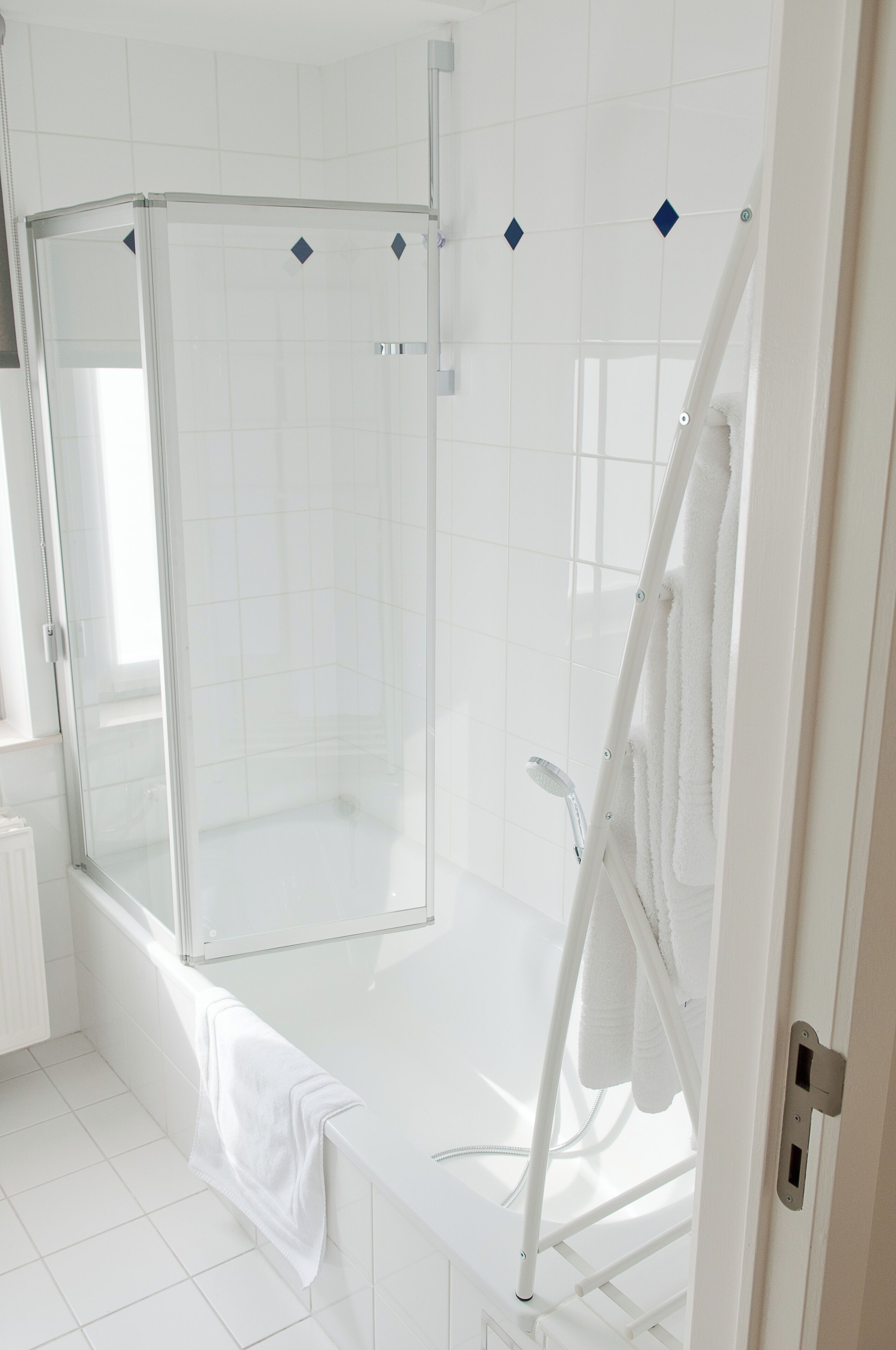 A modern bathroom with a glass-enclosed shower, a white bathtub, and a towel rack.