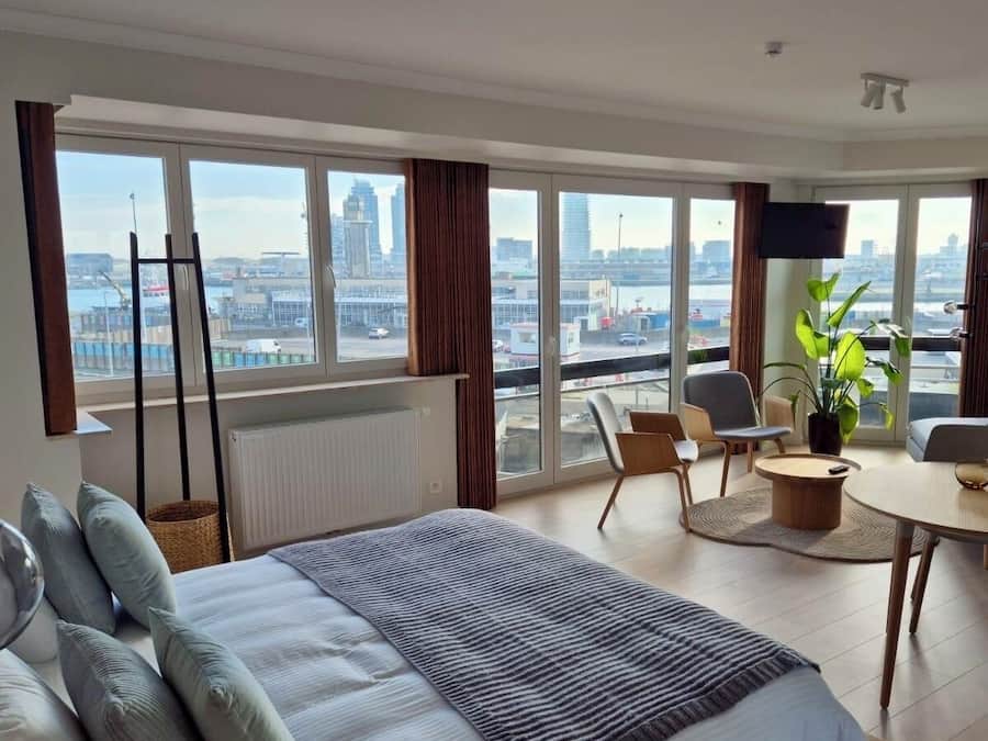 A modern hotel room with a large bed, a dining area, and a view of the cityscape.