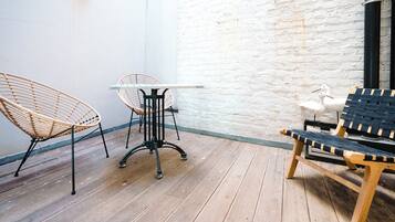 A wooden deck with wicker chairs and a table, white brick wall, and a wooden bench.