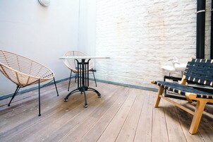 A wooden deck with wicker chairs and a table, white brick wall, and a wooden bench.