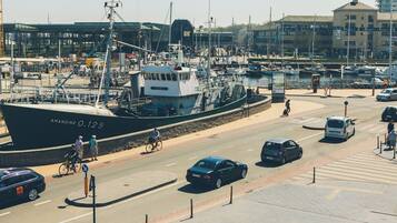 A harbor with a large ship docked, a road with cars and bicycles, and buildings in the background.