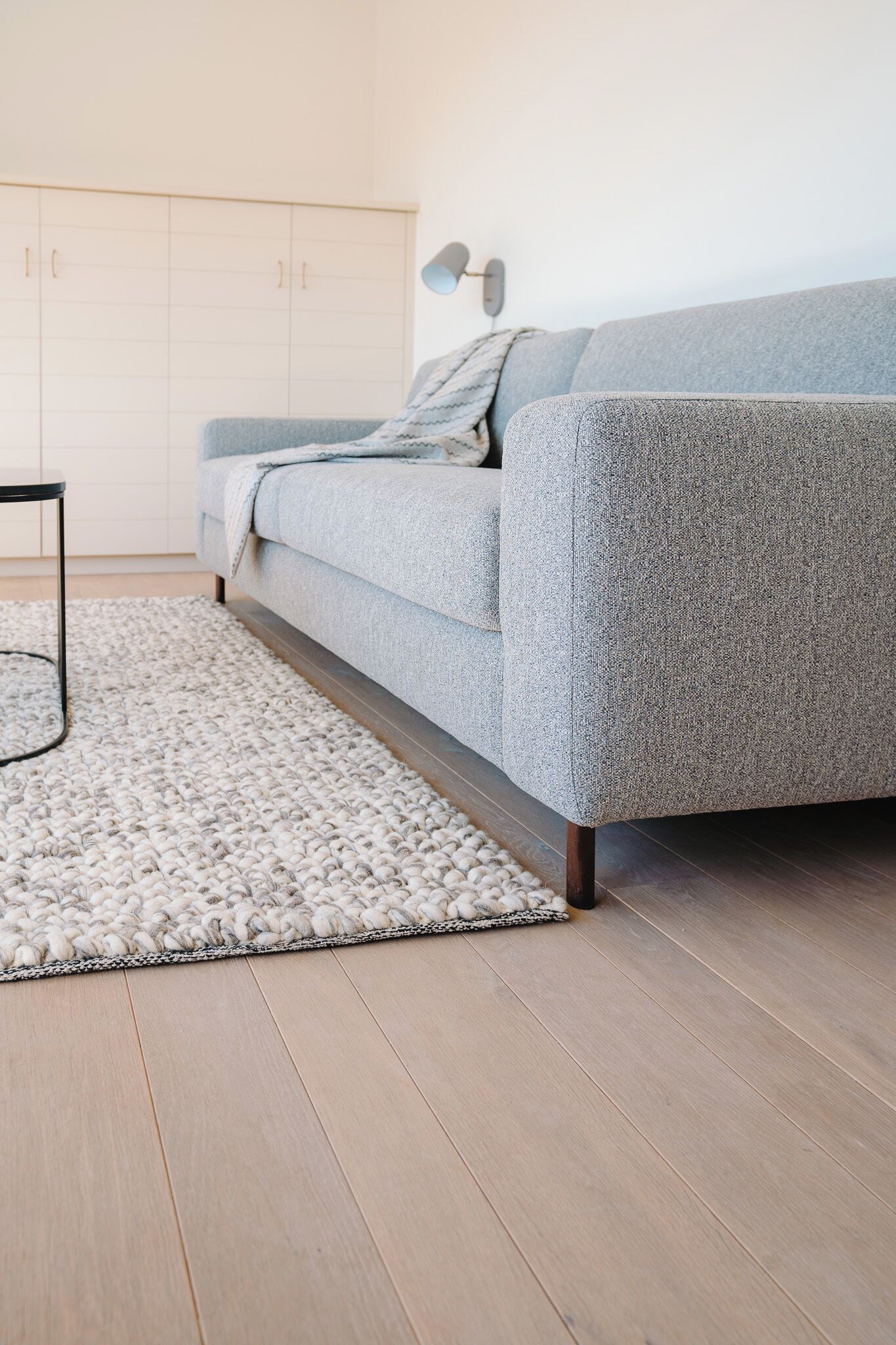 Een moderne woonkamer met een grijze bank, een wit vloerkleed, houten vloeren en een witte inbouwkast.
