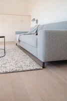 Ein modernes Wohnzimmer mit grauem Sofa, einem weißen Teppich, Holzboden und einem weißen Kleiderschrank.