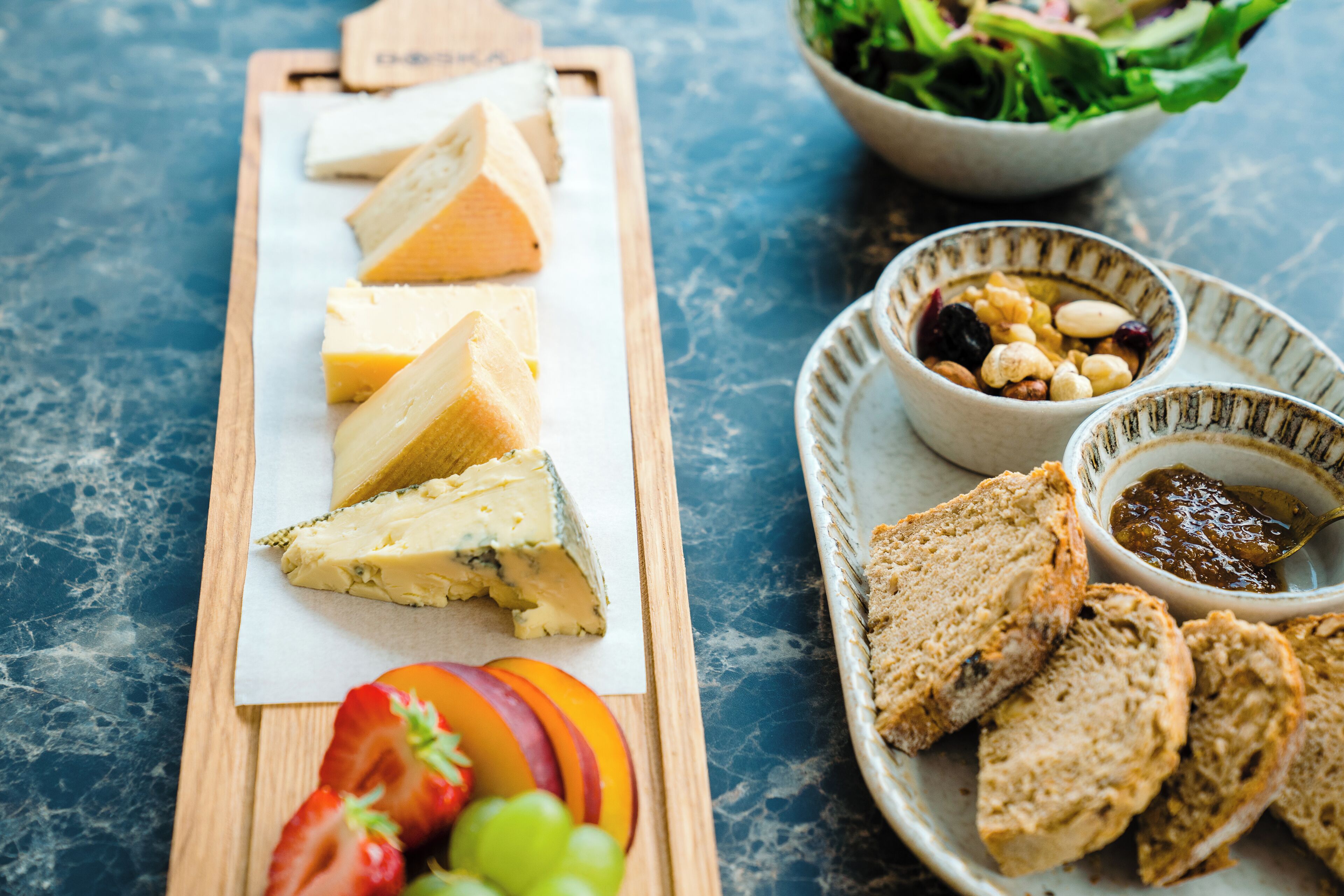 Una tabla de quesos con varios tipos de queso, uvas y pan sobre una tabla de madera.