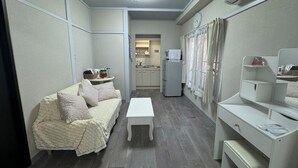 A compact living space with a sofa, a small table, a kitchenette, and a mirror. - Kobayashi Building (Tokyo)