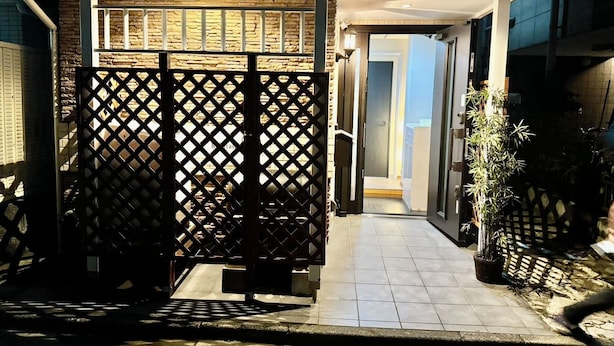 A modern entrance with a stone facade, a wooden lattice gate, and a tiled pathway leading to a door. - Kobayashi Building (Tokyo)