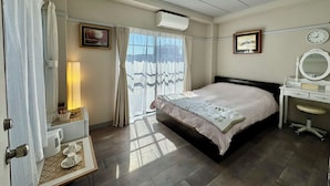 A hotel room with a bed, bedside table, lamp, air conditioning unit, and a window with curtains. - Kobayashi Building (Tokyo)