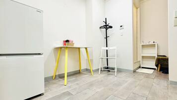 A small, clean room with a white refrigerator, a yellow table, a white shelf, and a black coat rack.