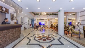 Een hotel lobby met een receptiebalie, een kroonluchter, een televisie en een eetgedeelte.