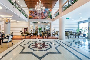 A spacious lobby with a high ceiling, a central chandelier, and a colorful mural. - Otel Kaya (Izmir)