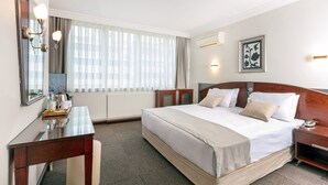 Een hotelkamer met een groot bed, een bureau, een spiegel en een raam met gordijnen.