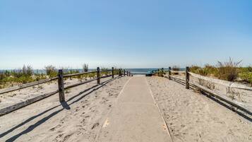 A sandy beach path with wooden railings leading to the ocean.