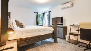 A bedroom with a bed, bedside table, lamp, desk, chair, and an air conditioning unit. - 4 Mi to Nyc, Shared Yard: Englewood Apartment! (Englewood)