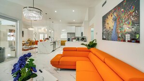 En moderne stue med en stor orange modulsofa, en lysekrone og et farverigt påfuglmotiv på væggen.