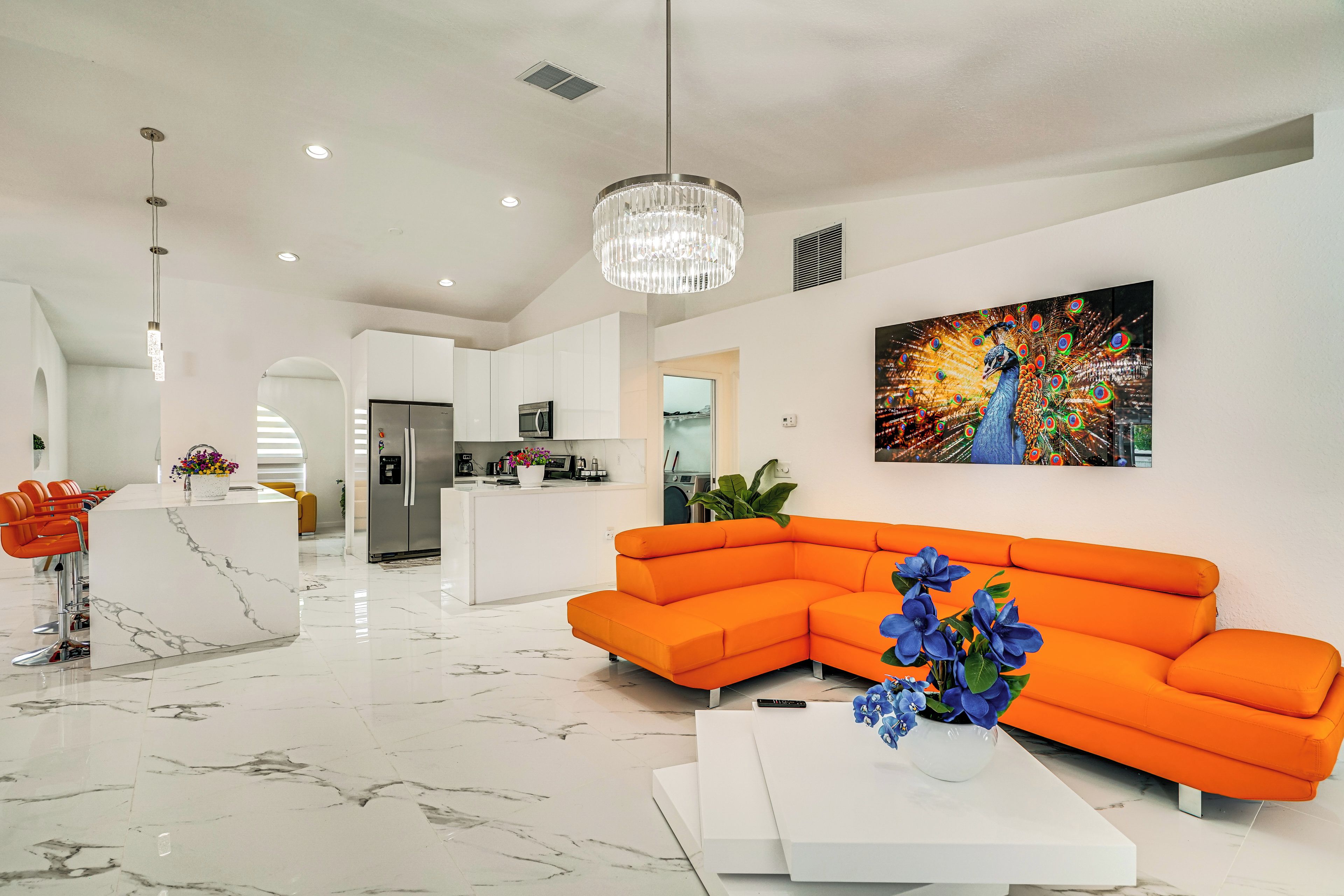 A modern living room with a white marble floor, a large orange sectional sofa, a white coffee table, and a chandelier.