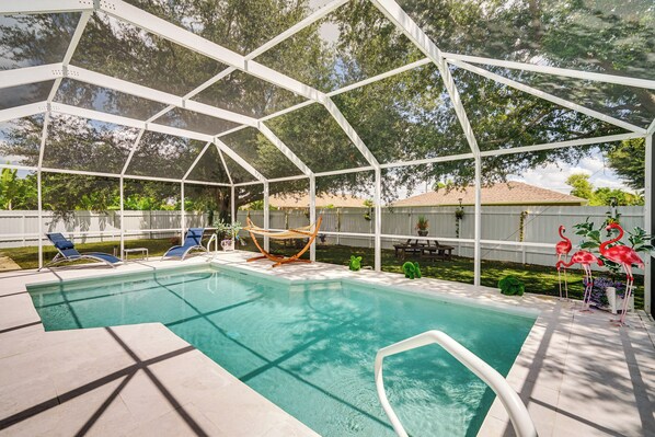 A covered swimming pool with a white roof, surrounded by lounge chairs and flamingo decorations. - Cape Coral Pool Home w/ Outdoor Kitchen & Games (Cape Coral)