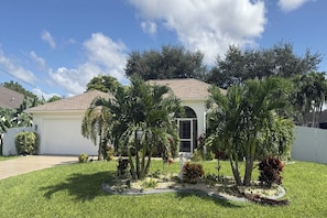 A residential house with a garage, surrounded by well-maintained grass and palm trees.