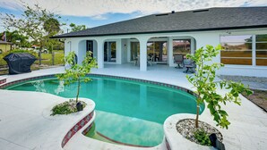 Ein Schwimmbad mit überdachter Terrasse, einem kleinen Garten und Blick auf ein Wohngebäude.