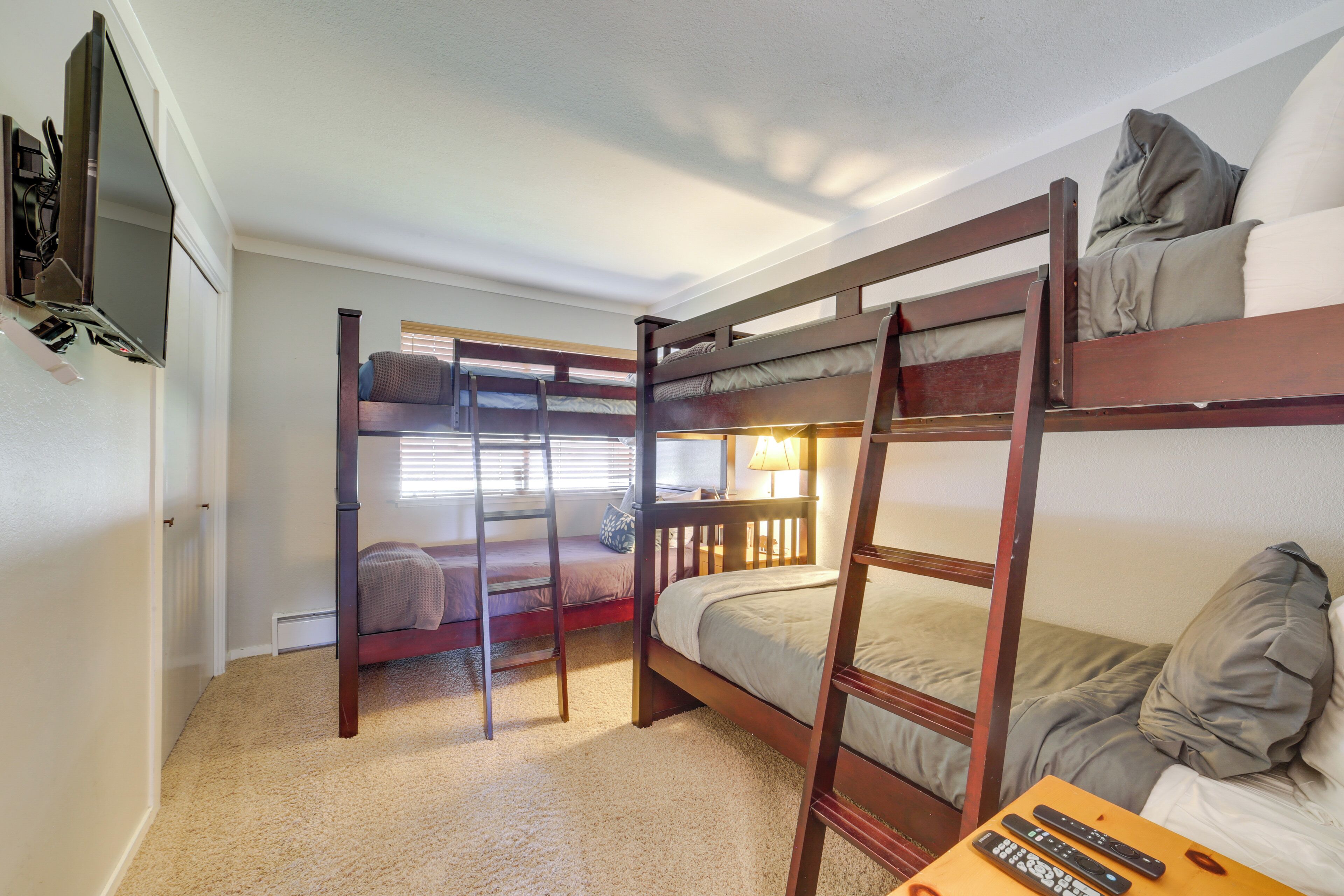 A bunk bed room with a TV on the wall, a ladder, and a table with remote controls.