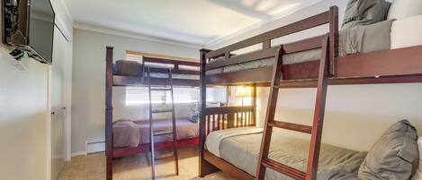 A bunk bed room with a TV on the wall, a ladder, and a table with remote controls.