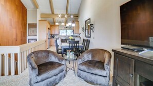 A spacious living area with a high ceiling, wooden beams, a dining table with chairs, a small round table with a vase, and a television on a wooden cabinet. - Walk to Ski Lift: Mtn-view Condo in Mammoth Lakes (Mammoth Lakes)