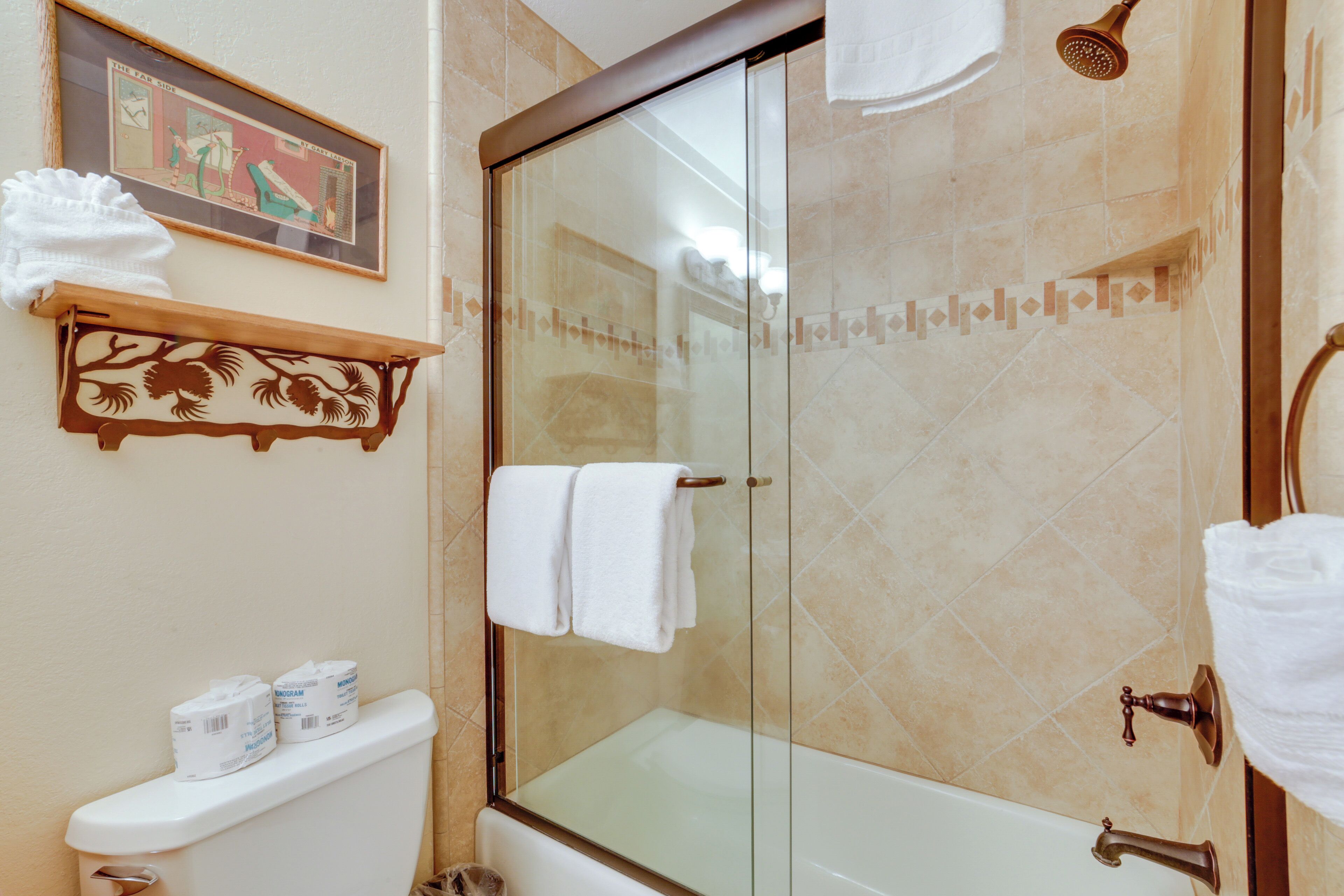 A bathroom with a glass-enclosed shower, a toilet with a shelf holding toilet paper, and a framed picture on the wall.