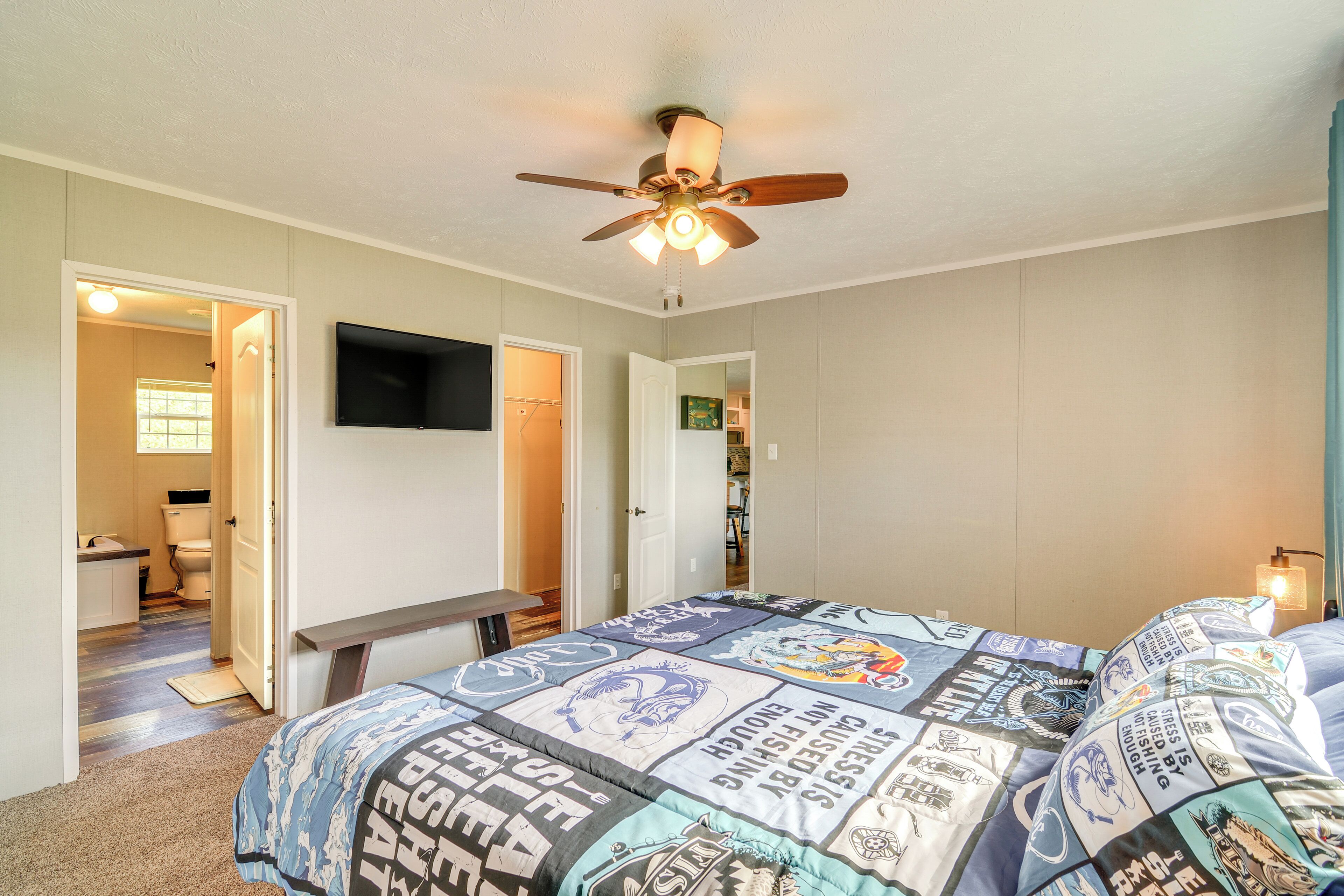 A bedroom with a bed, a ceiling fan, a TV, and a desk.