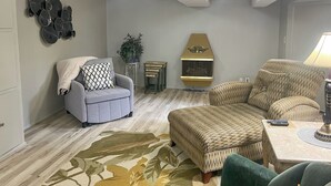 A living room with a grey sofa, a patterned ottoman, a green armchair, a wooden coffee table, and a decorative wall piece. - < 1 Mi to Lambeau Field: Green Bay Home w/ Grill! (Green Bay)