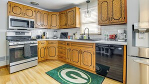 A modern kitchen with wooden cabinets, stainless steel appliances, and a green rug with a logo. - < 1 Mi to Lambeau Field: Green Bay Home w/ Grill! (Green Bay)