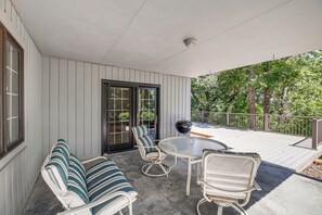A covered patio with a glass-top table, two striped sofas, and a grill.