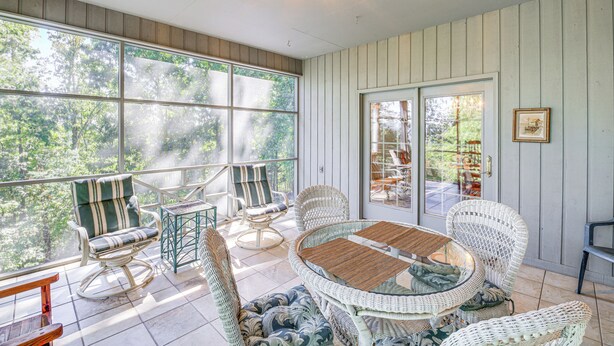 A sunlit room with wicker furniture, large windows, and a view of greenery outside. - Spacious Home w/ Hiking Trail Access in Bristol! (Bristol)