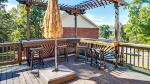 Un terrazzo in legno con una pergola, sedute all'aperto e un oggetto cilindrico alto.