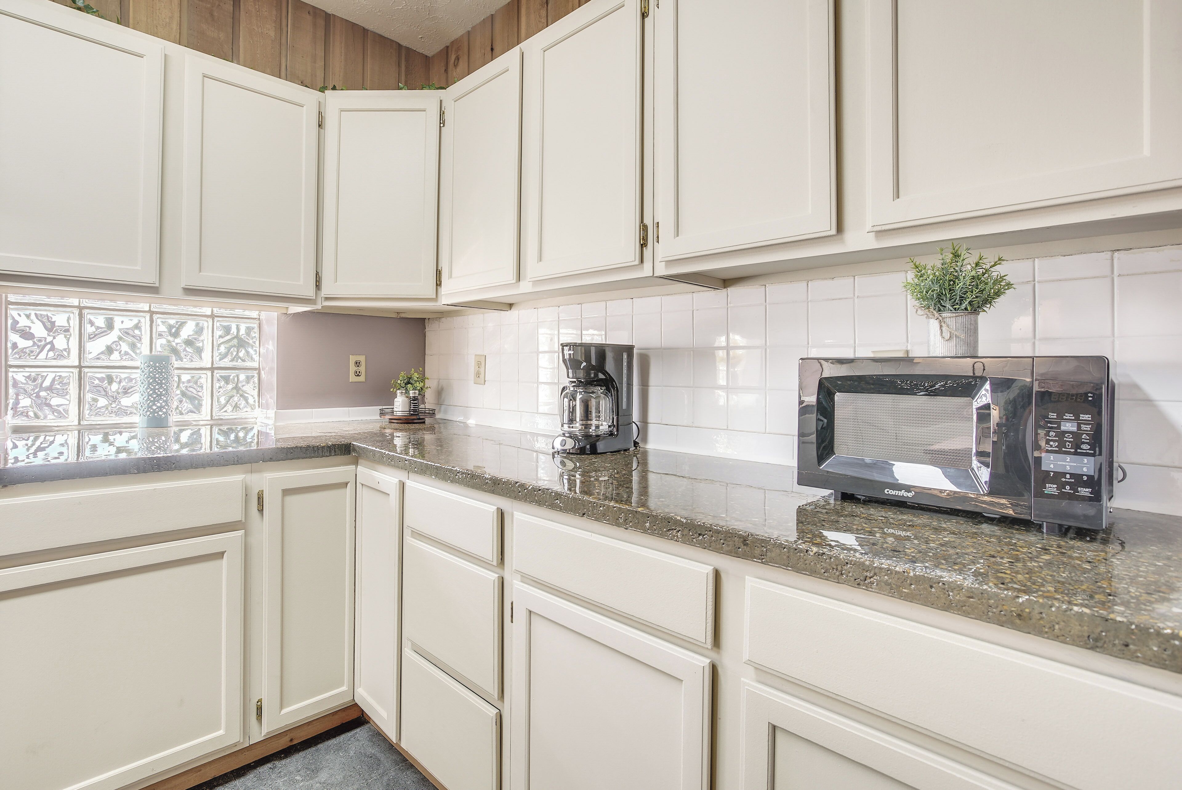 A kitchen with white cabinets, a granite countertop, a coffee maker, and a microwave.
