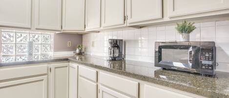A kitchen with white cabinets, a granite countertop, a coffee maker, and a microwave.