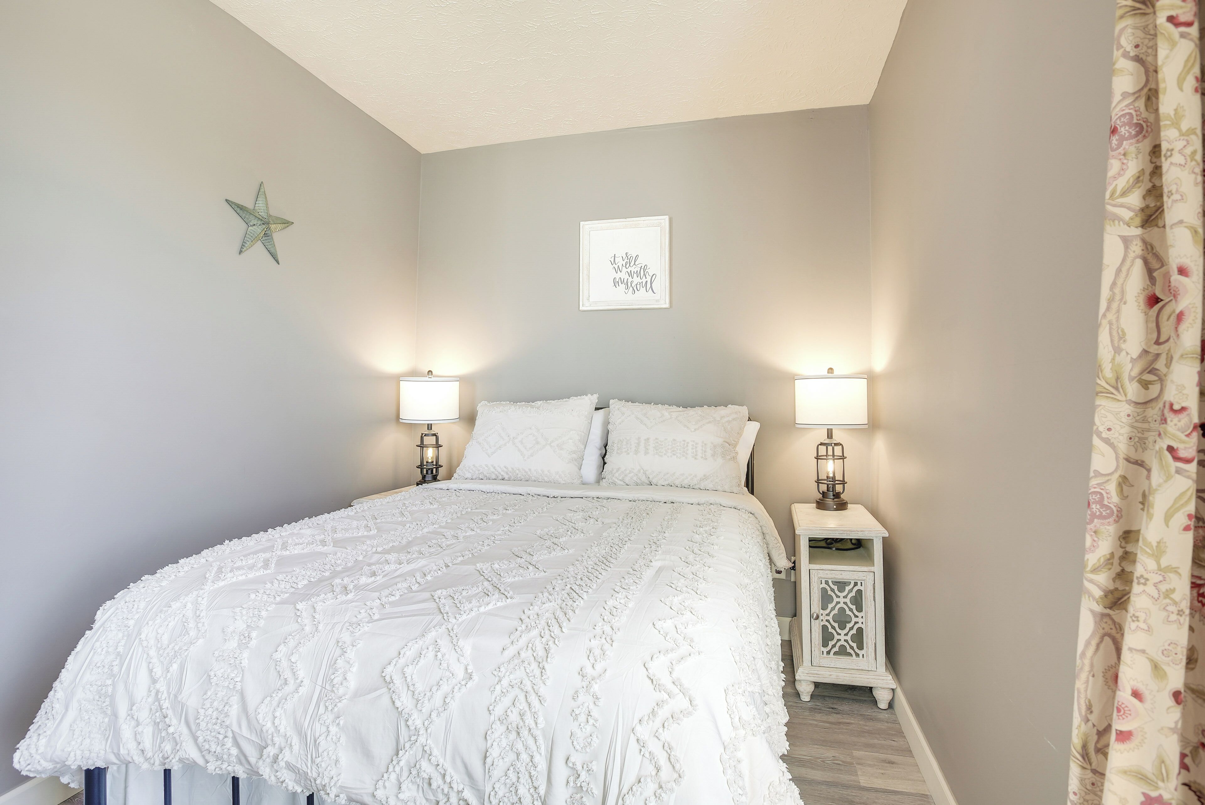 Une chambre avec un grand lit, deux tables de chevet avec des lampes, une décoration en forme d’étoile sur le mur et une citation encadrée.