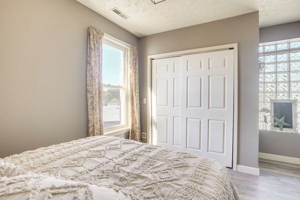 Un dormitorio con una cama grande, una ventana con cortinas, una puerta blanca y vistas al exterior.