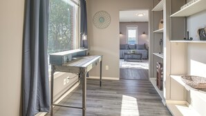 A hallway with a desk, shelves, and a view into a living area.