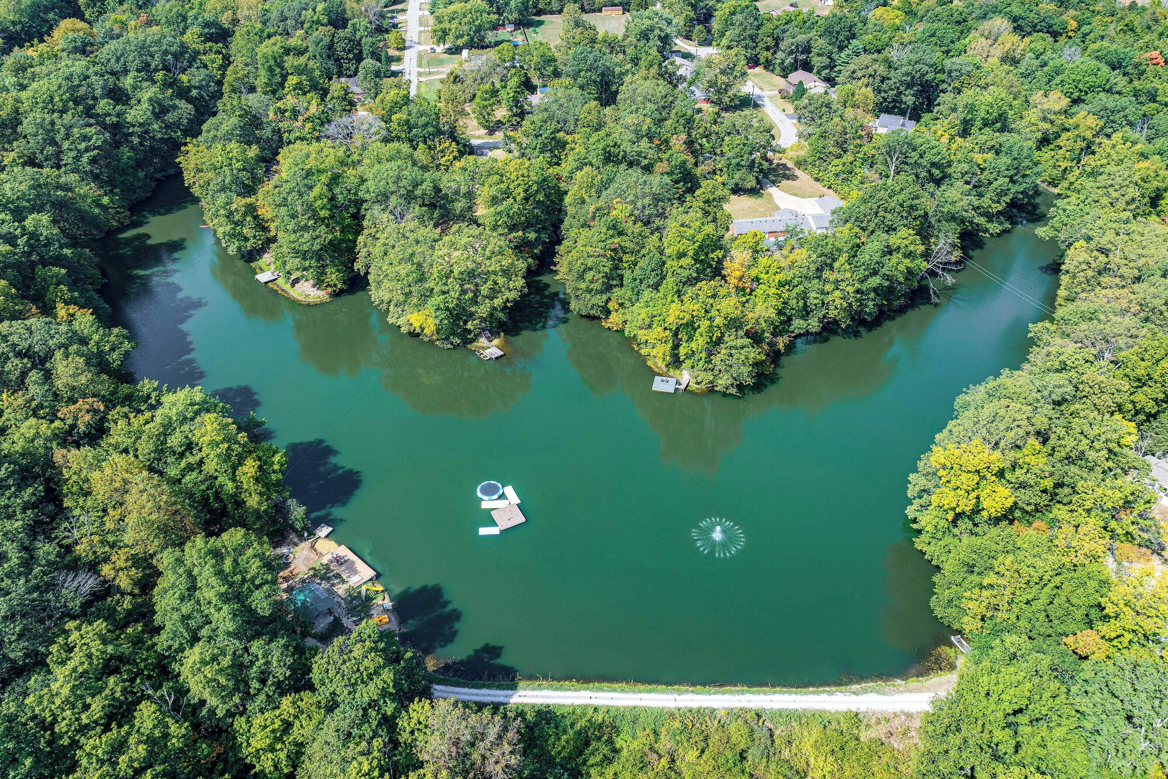 Une vue aérienne d’un lac entouré d’une forêt dense, avec un petit quai et un bateau.