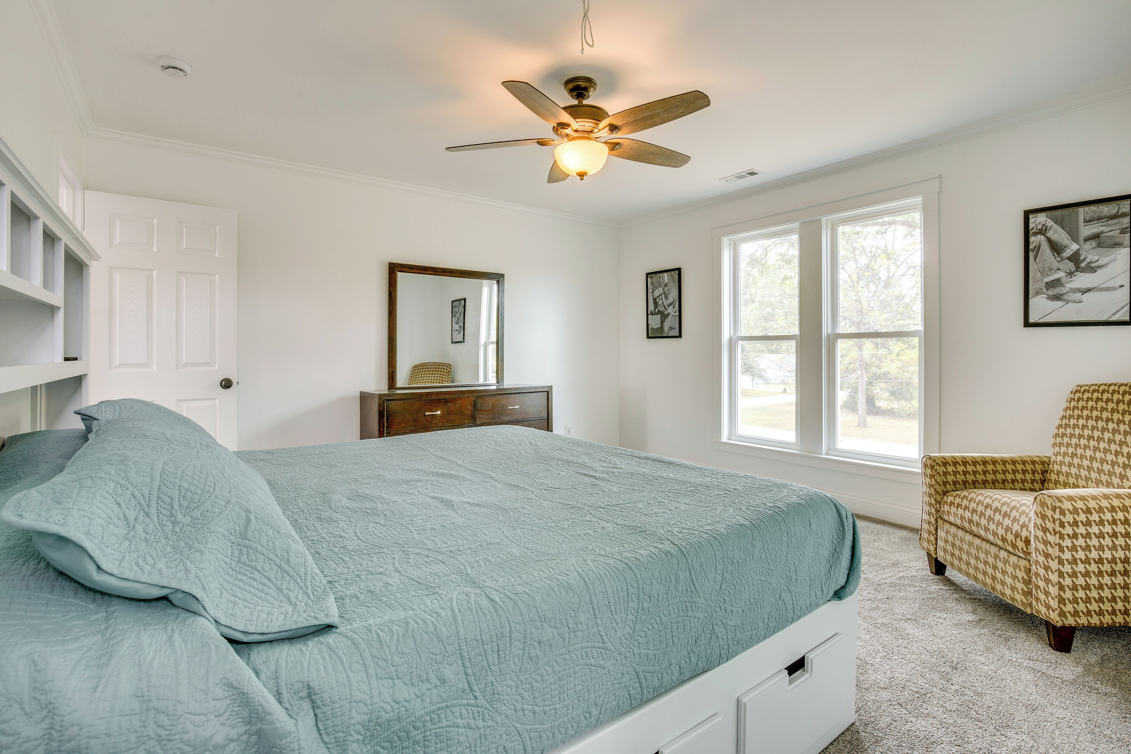 Une chambre à coucher comprenant un lit, un ventilateur de plafond, une commode, une chaise et une grande fenêtre.