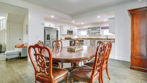 A dining area with a round table and wooden chairs, a kitchen in the background, and a large wooden cabinet. - Walk to Winery: Family-friendly Holt Getaway (Holt)