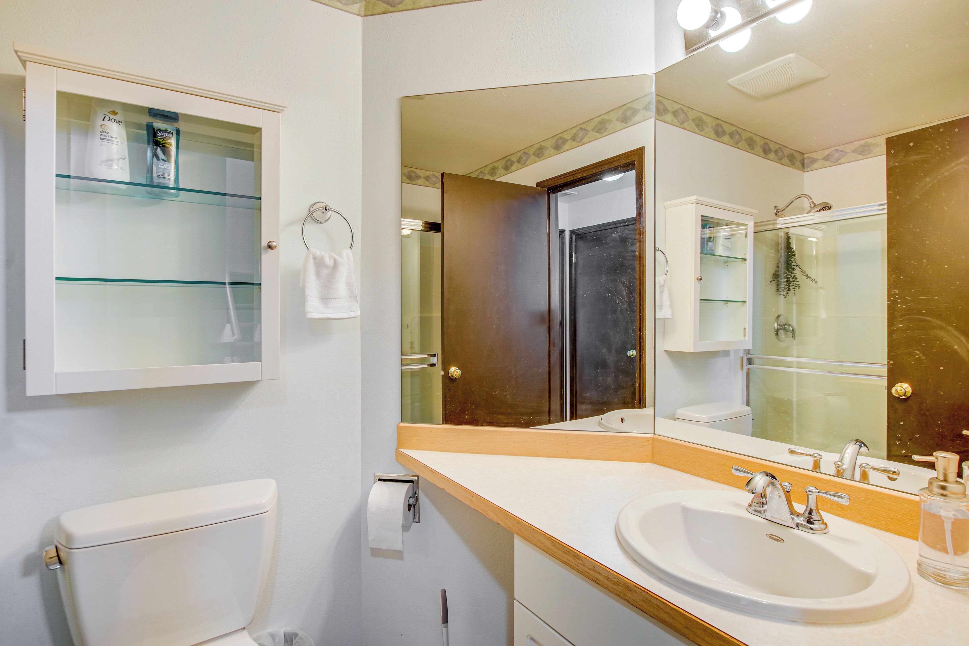 Een badkamer met een toilet, een wastafel met spiegel en een glazen kastje boven het toilet.