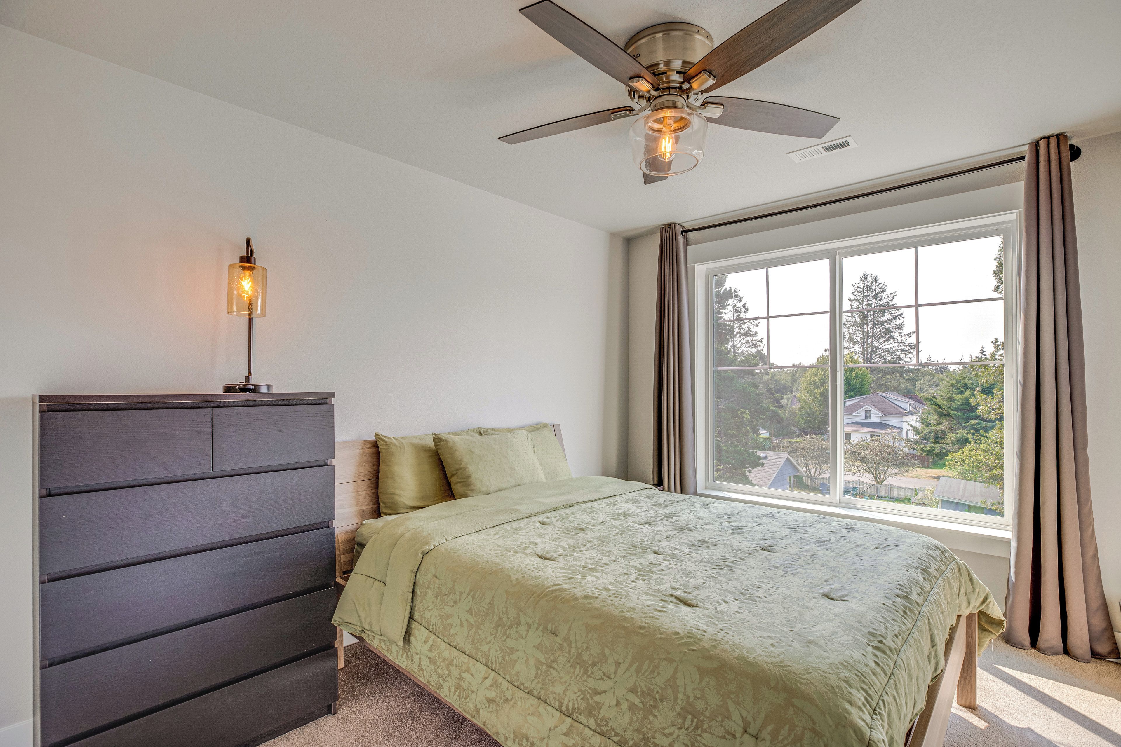 A bedroom with a bed, a dresser, a ceiling fan, and a window with curtains.