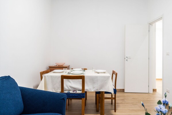 A dining area with a table set for four, wooden chairs, a blue sofa, and a white door. - The Flower House by Wonderful Italy (Bitritto)